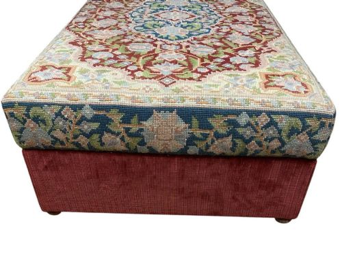 fig 3. A low rectangular ottoman featuring a central multi-coloured floral needlepoint tapestry top bordered by red velvet side fabric with a pull tab.