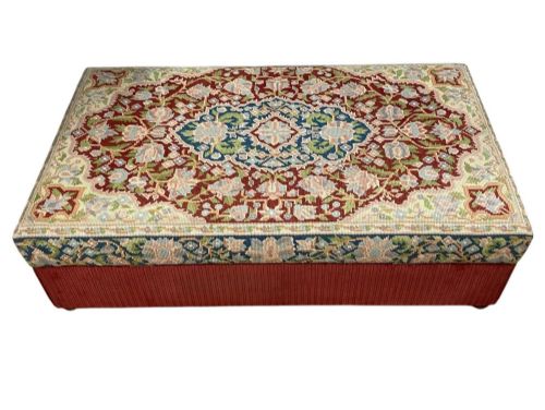 fig 4. A low rectangular ottoman featuring a central multi-coloured floral needlepoint tapestry top bordered by red velvet side fabric with a pull tab.