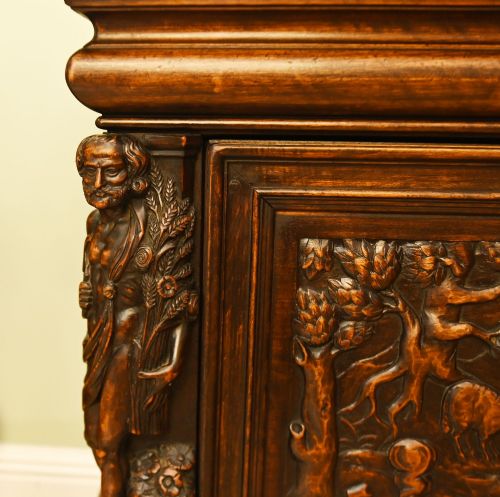 fig 1. A carved dark walnut coffer featuring a central relief scene flanked by carved corner figures and decorative egg-and-dart base mouldings.