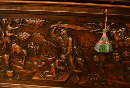 fig 3. A carved dark walnut coffer featuring a central relief scene flanked by carved corner figures and decorative egg-and-dart base mouldings.