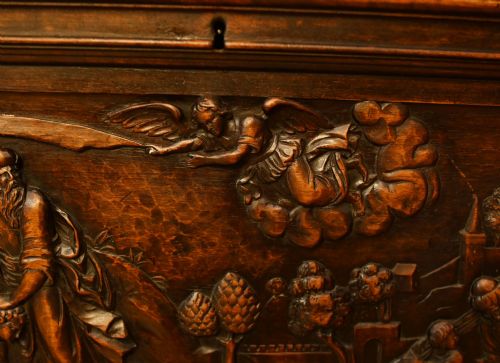 fig 4. A carved dark walnut coffer featuring a central relief scene flanked by carved corner figures and decorative egg-and-dart base mouldings.