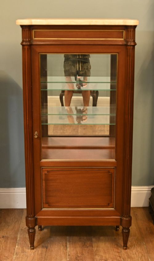 fig 1. A French Directoire style mahogany vitrine cabinet featuring a single glazed door, fluted corner pilasters, brass line inlays, tapered turned feet, and a marble top surface.