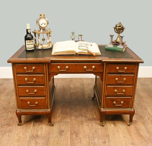 fig 1. An antique French Empire mahogany kneehole desk featuring a green leather inset writing surface, nine drawers with brass handles, and brass castors.