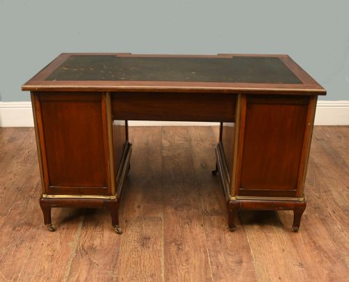 fig 2. An antique French Empire mahogany kneehole desk featuring a green leather inset writing surface, nine drawers with brass handles, and brass castors.