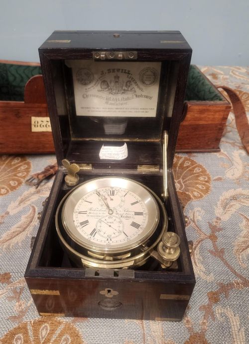 fig 2. A Victorian brass marine chronometer mounted inside a brass-bound dark mahogany box with a printed manufacturer label.