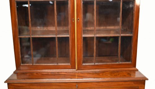 fig 2. A Georgian mahogany secretaire bookcase featuring a glazed upper cabinet, a pull-out secretaire drawer with brass oval handles, and lower panelled doors.