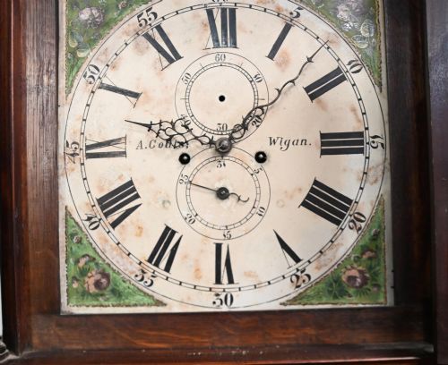 fig 2. A Georgian mahogany longcase clock featuring a swan-neck pediment with three brass finials, a painted dial with Roman numerals, and a flame mahogany door.