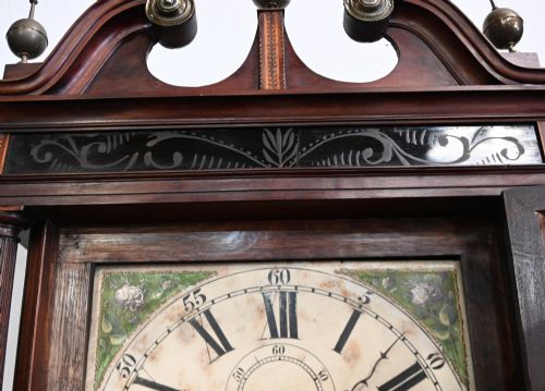 fig 3. A Georgian mahogany longcase clock featuring a swan-neck pediment with three brass finials, a painted dial with Roman numerals, and a flame mahogany door.