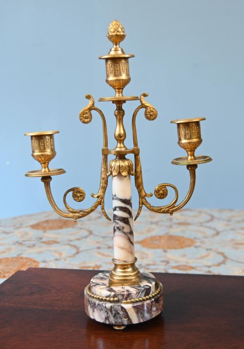 fig 2. A late nineteenth-century French clock garniture set featuring a central portico clock in purple-veined white marble with gilt bronze mounts, flanked by two matching two-light candelabras.