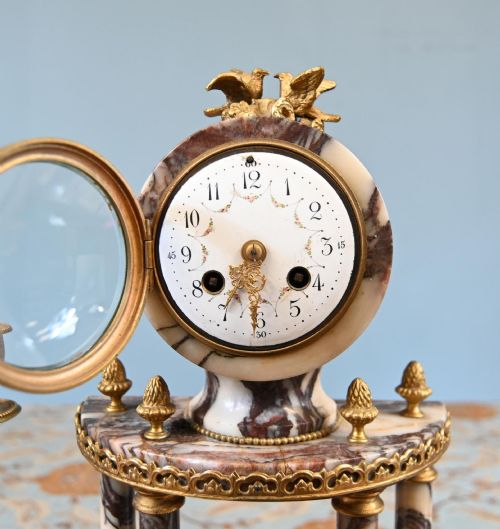 fig 3. A late nineteenth-century French clock garniture set featuring a central portico clock in purple-veined white marble with gilt bronze mounts, flanked by two matching two-light candelabras.