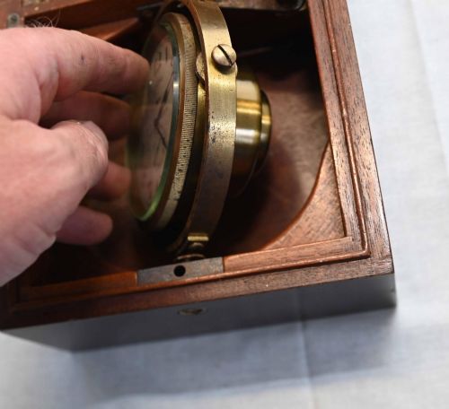fig 1. A 1920s Longines marine chronometer clock with a white dial set in a brass gimbal mechanism inside an open mahogany box.
