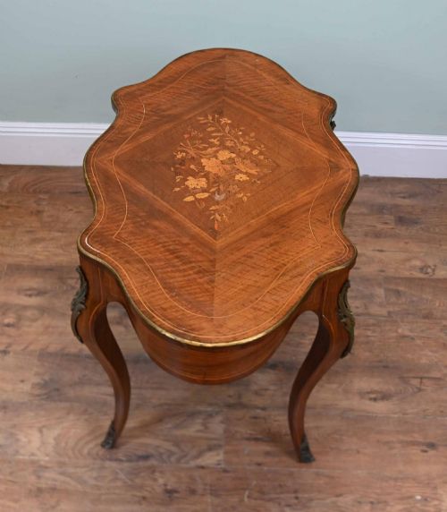 fig 1. A French Louis XV style writing desk crafted from brown wood with a serpentine top, floral marquetry inlay, cabriole legs, and brass mounts.