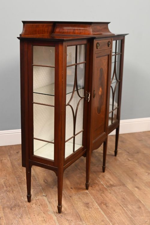 fig 1. An Edwardian inlaid mahogany display cabinet featuring astragal glazed side doors, a central wooden cupboard with oval marquetry, and slender square tapered legs.