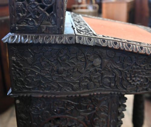 fig 2. A dark hardwood Burmese Davenport desk with pierced carved floral decoration, an openwork gallery, and a terracotta leather writing surface.
