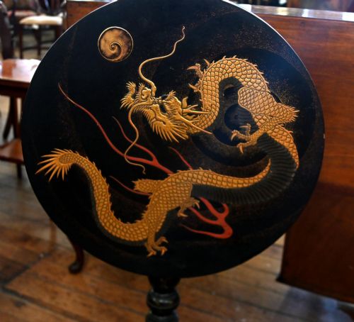 fig 2. A black lacquered circular tilt-top side table featuring a gilt dragon motif, supported on a turned central column and tripod pedestal legs.