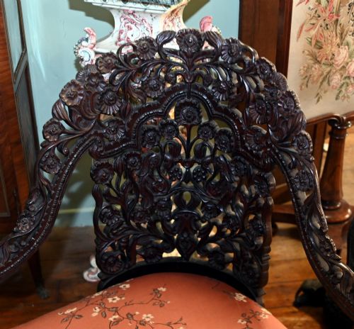 fig 2. An intricately carved 19th-century dark teak sofa featuring openwork floral motifs and a terracotta floral upholstered seat pad.