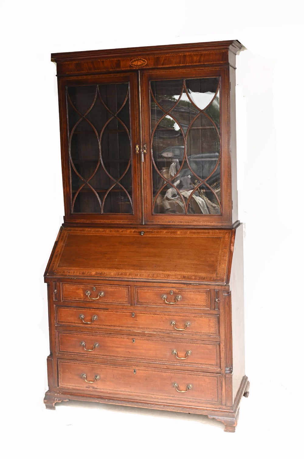 A late 18th-century mahogany bureau bookcase featuring upper astragal glazed double doors with an oval shell marquetry pediment, above a slanted fall-front writing desk and four graduating drawers with brass handles.