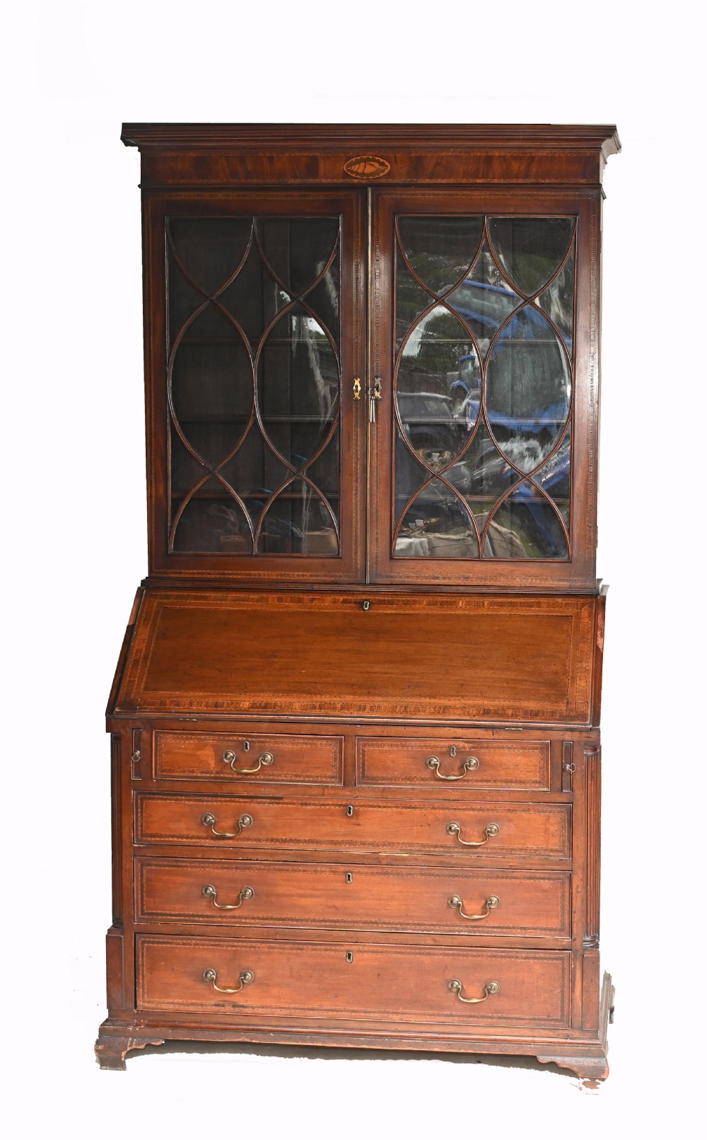 A late 18th-century mahogany bureau bookcase featuring upper astragal glazed double doors with an oval shell marquetry pediment, above a slanted fall-front writing desk and four graduating drawers with brass handles. View II