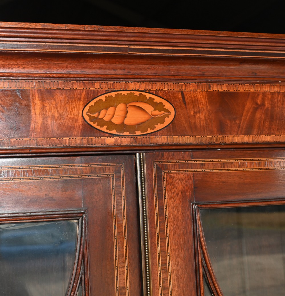 A late 18th-century mahogany bureau bookcase featuring upper astragal glazed double doors with an oval shell marquetry pediment, above a slanted fall-front writing desk and four graduating drawers with brass handles. View V
