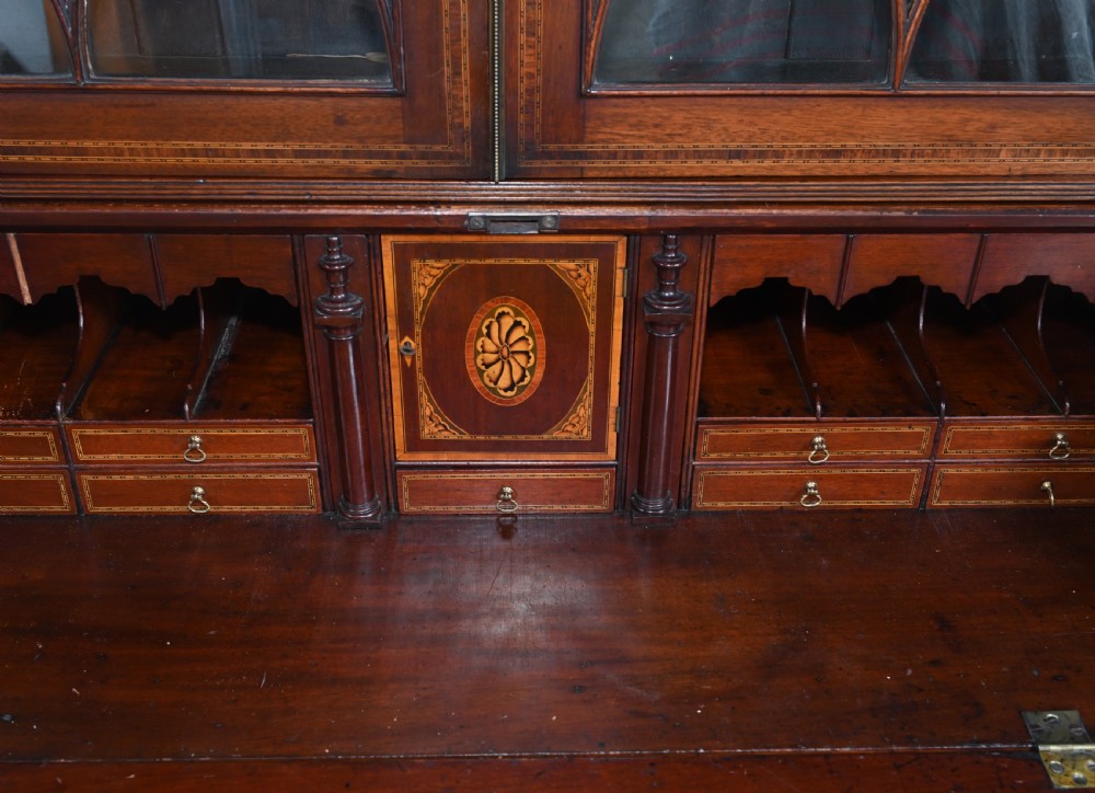 A late 18th-century mahogany bureau bookcase featuring upper astragal glazed double doors with an oval shell marquetry pediment, above a slanted fall-front writing desk and four graduating drawers with brass handles. View VII