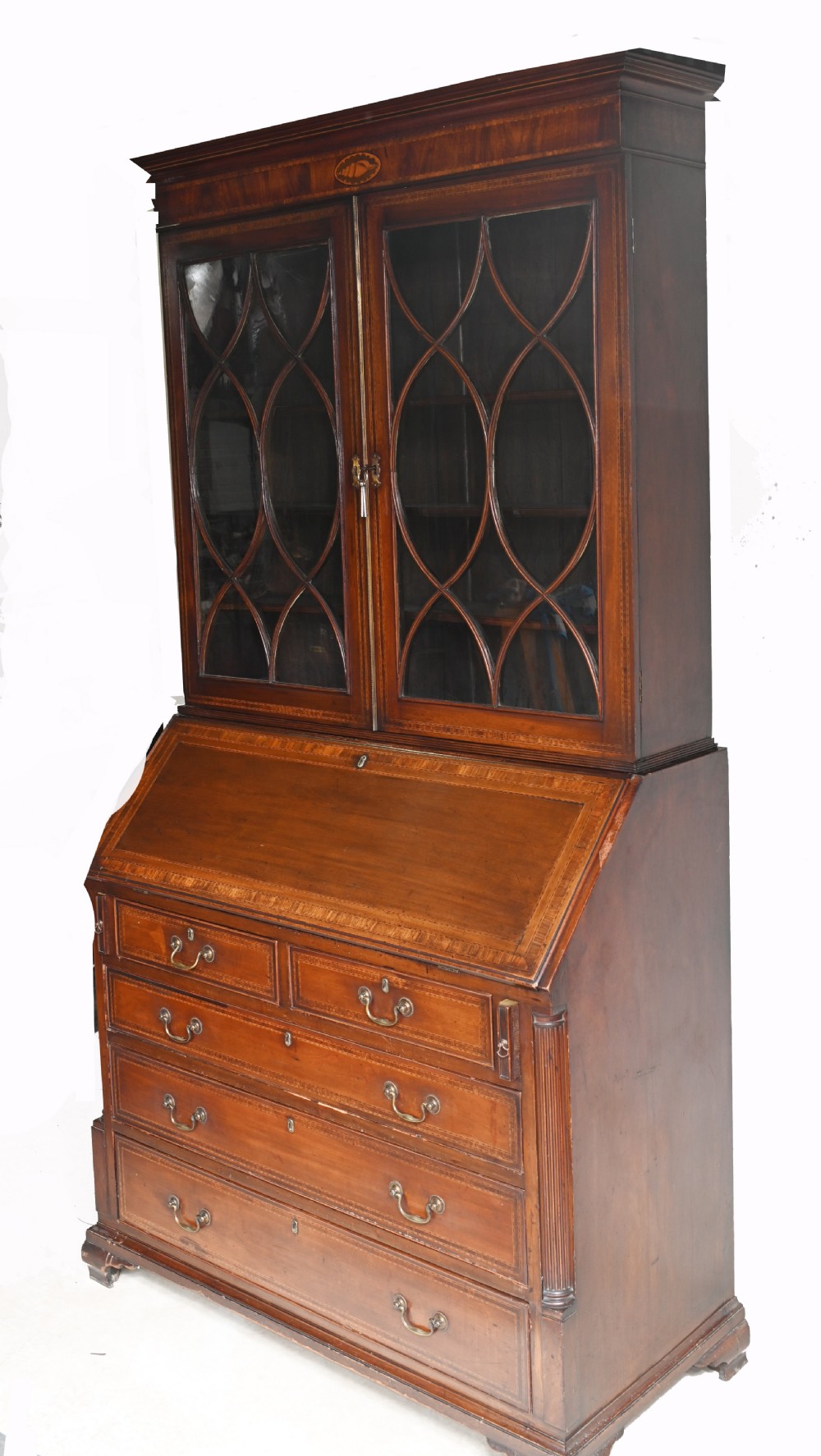 A late 18th-century mahogany bureau bookcase featuring upper astragal glazed double doors with an oval shell marquetry pediment, above a slanted fall-front writing desk and four graduating drawers with brass handles. View IX