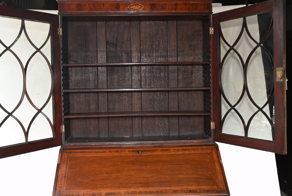 A late 18th-century mahogany bureau bookcase featuring upper astragal glazed double doors with an oval shell marquetry pediment, above a slanted fall-front writing desk and four graduating drawers with brass handles. View XI