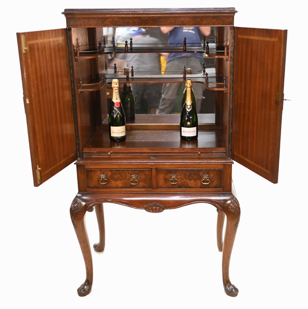 An Art Deco burr walnut drinks cabinet on a carved cabriole leg stand with ornate brass hardware and two lower drawers. View V