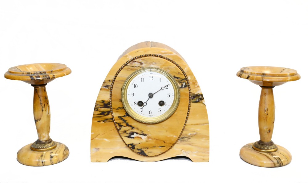 An antique French three-piece garniture set featuring an arched yellow veined marble clock flanked by two matching marble pedestal tazzas.