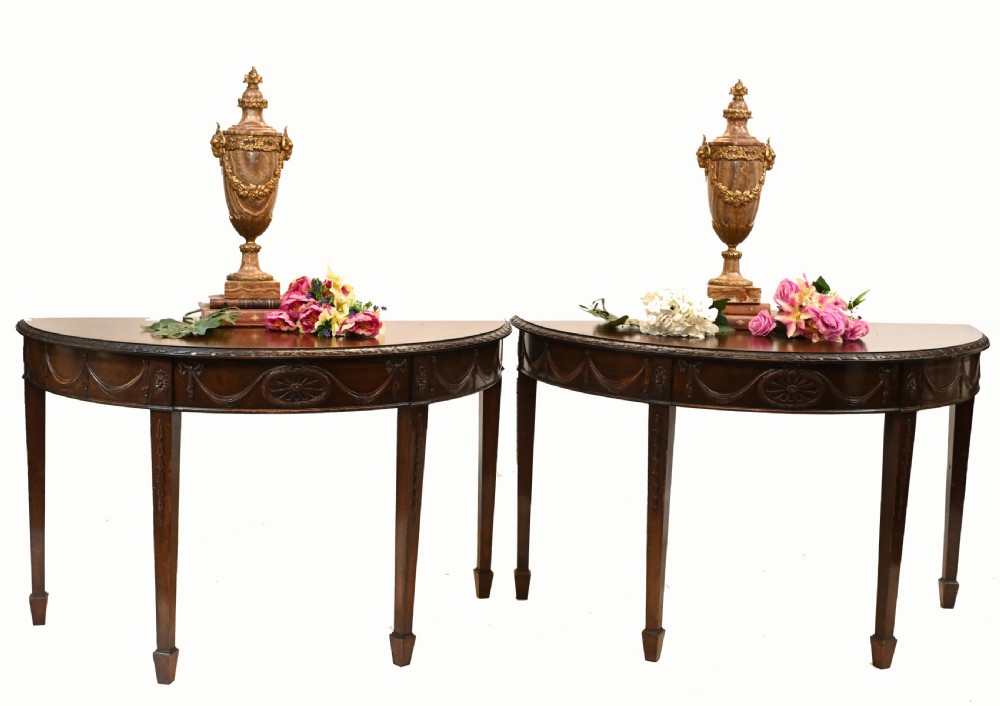 A pair of demilune mahogany console tables featuring carved friezes with decorative swags and oval paterae, supported by tapered square legs. View III