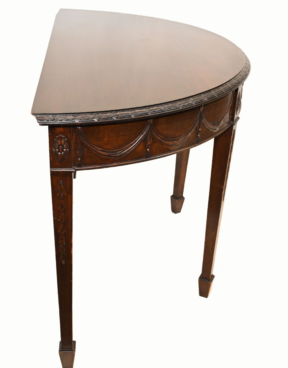 A pair of demilune mahogany console tables featuring carved friezes with decorative swags and oval paterae, supported by tapered square legs. View IX