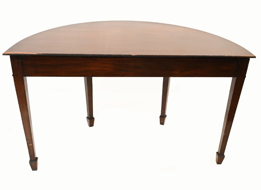 A pair of demilune mahogany console tables featuring carved friezes with decorative swags and oval paterae, supported by tapered square legs. View X