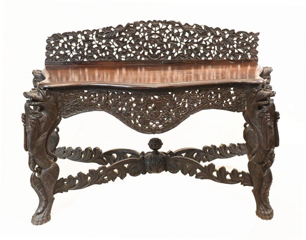 An intricately carved dark teak Burmese console table featuring a pierced foliate gallery back, detailed apron, sculpted mythical beast legs, and a carved lower stretcher.