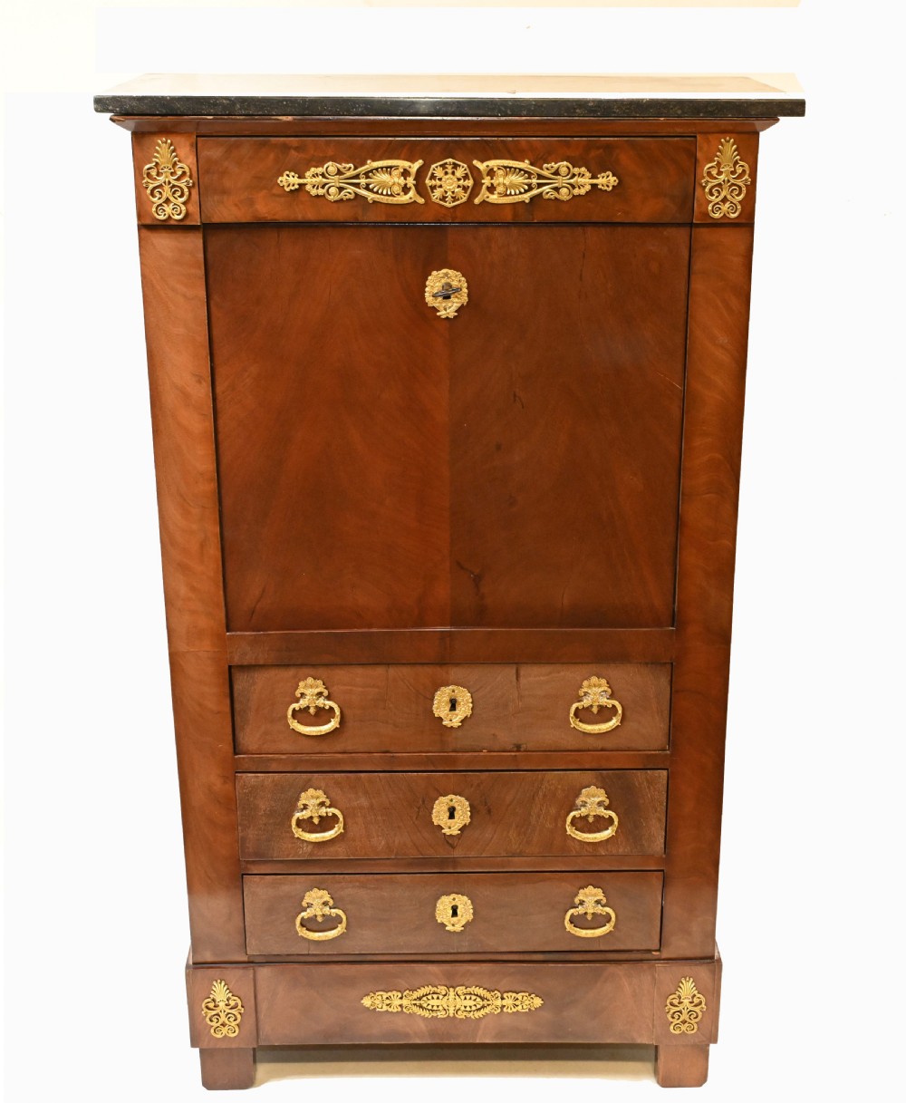 A late 19th-century French Empire mahogany escritoire desk featuring a dark marble top, drop-front writing compartment, three lower drawers, and ornamental gilt-bronze mounts.