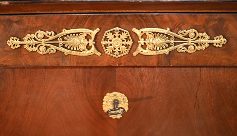 A late 19th-century French Empire mahogany escritoire desk featuring a dark marble top, drop-front writing compartment, three lower drawers, and ornamental gilt-bronze mounts. View II