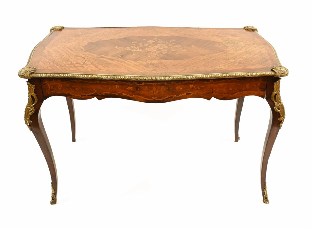 A French style writing table featuring floral marquetry wood veneers, cabriole legs, and ornate gilt-bronze mounts.
