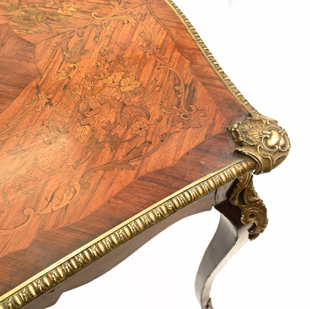 A French style writing table featuring floral marquetry wood veneers, cabriole legs, and ornate gilt-bronze mounts. View V