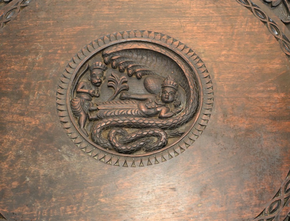 A circular dark carved teak side table featuring dense floral relief carving on the top and apron supported by a tripod base. View II