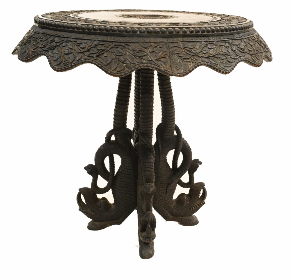 A circular dark carved teak side table featuring dense floral relief carving on the top and apron supported by a tripod base. View IV
