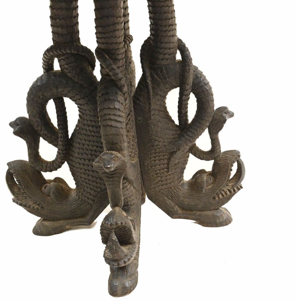 A circular dark carved teak side table featuring dense floral relief carving on the top and apron supported by a tripod base. View VI