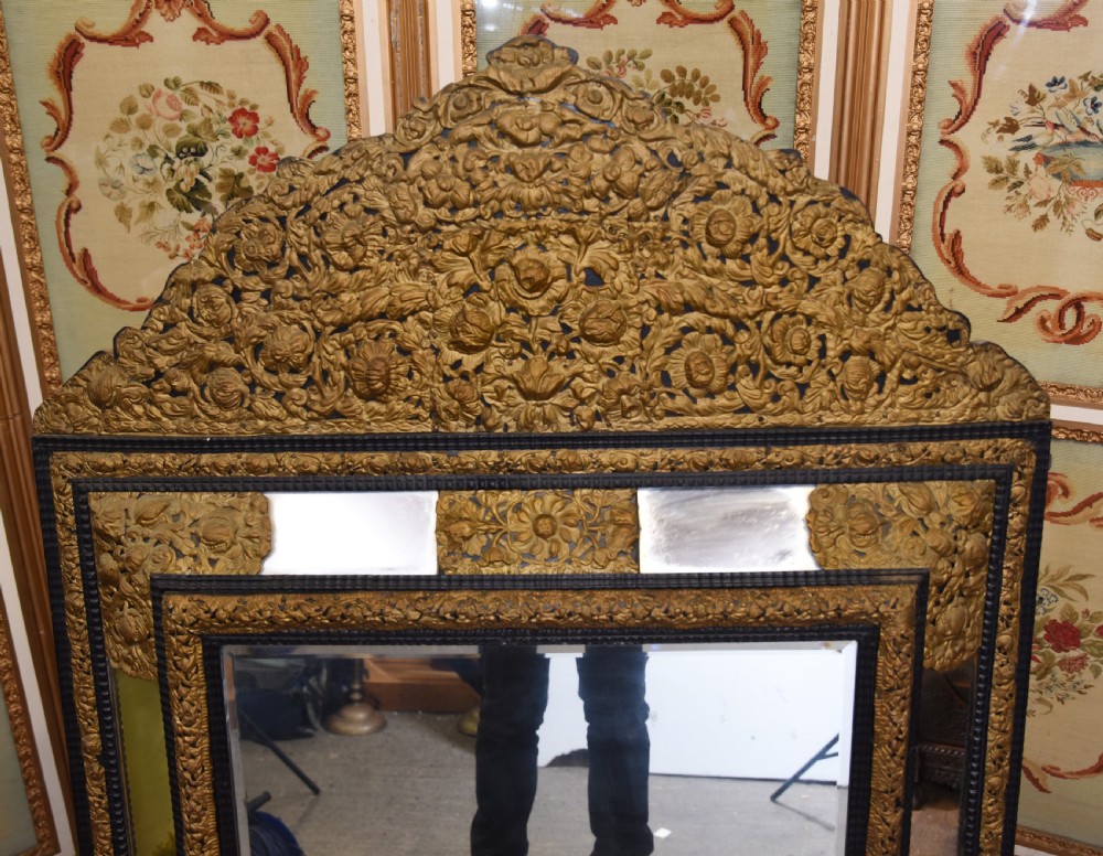 An antique French cushion mirror featuring an ornate repousse brass crest, detailed floral metal mounts, and a multi-panelled glass frame. View III