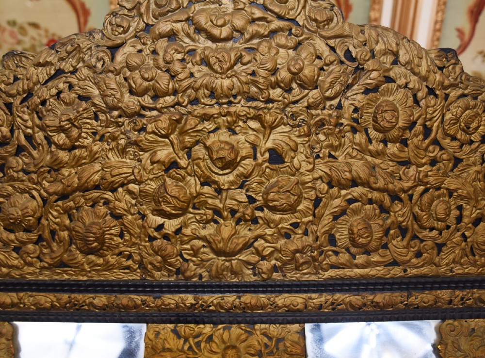 An antique French cushion mirror featuring an ornate repousse brass crest, detailed floral metal mounts, and a multi-panelled glass frame. View IV