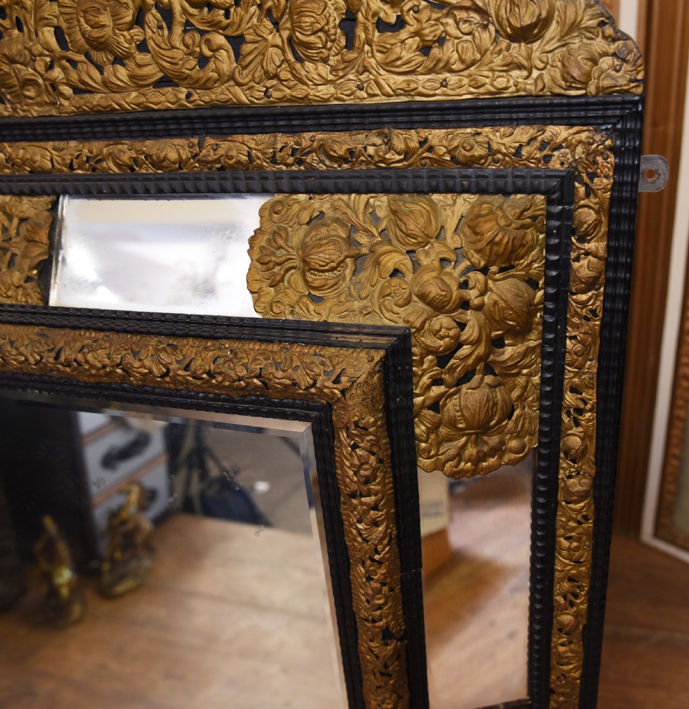 An antique French cushion mirror featuring an ornate repousse brass crest, detailed floral metal mounts, and a multi-panelled glass frame. View VI