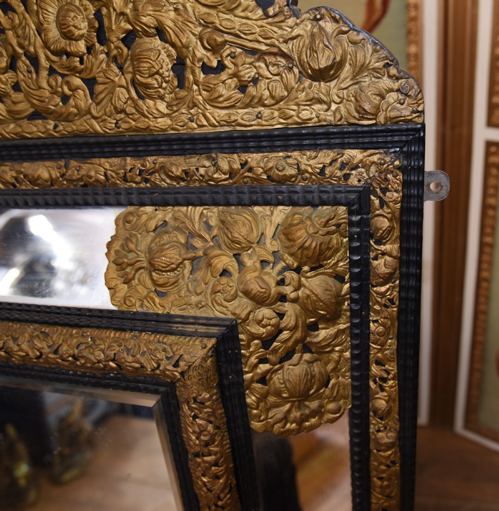 An antique French cushion mirror featuring an ornate repousse brass crest, detailed floral metal mounts, and a multi-panelled glass frame. View VII
