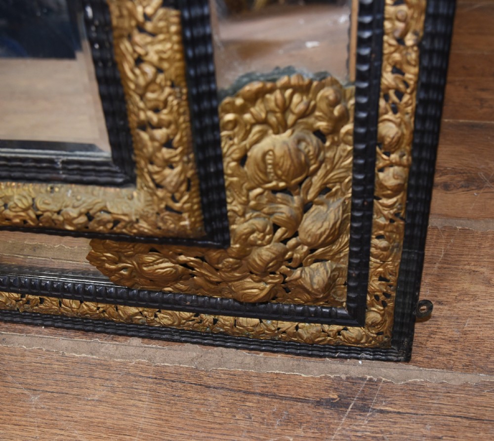 An antique French cushion mirror featuring an ornate repousse brass crest, detailed floral metal mounts, and a multi-panelled glass frame. View IX