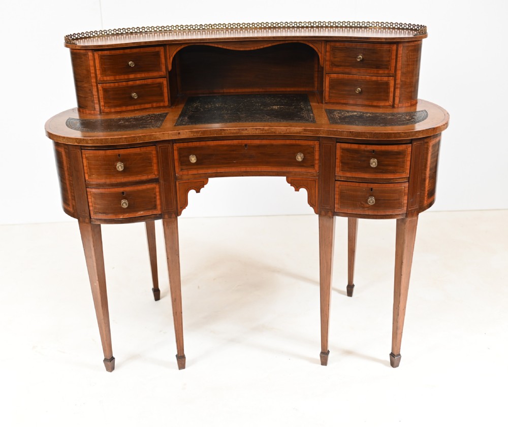 An Edwardian mahogany kidney-shaped writing desk featuring a brass gallery top, inlaid drawers, black leather writing inserts, and tapered legs.