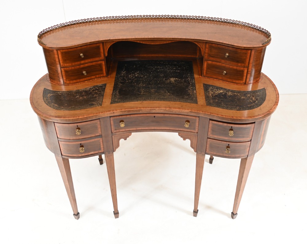 An Edwardian mahogany kidney-shaped writing desk featuring a brass gallery top, inlaid drawers, black leather writing inserts, and tapered legs. View II