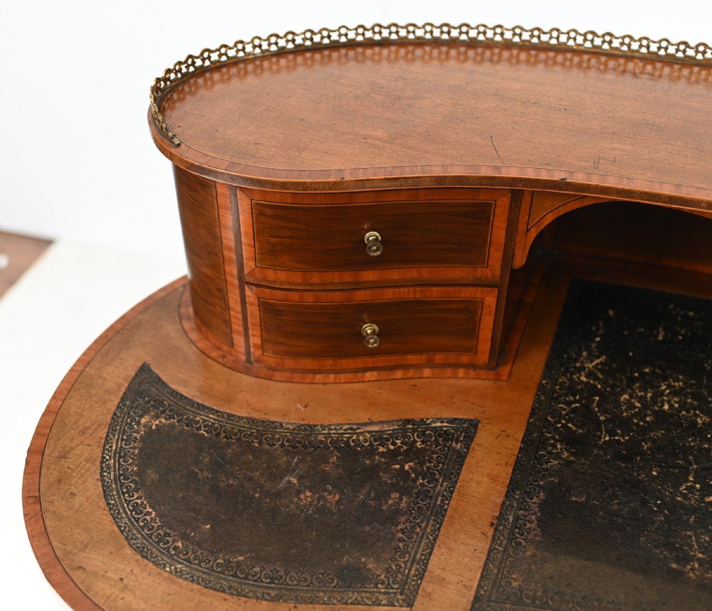 An Edwardian mahogany kidney-shaped writing desk featuring a brass gallery top, inlaid drawers, black leather writing inserts, and tapered legs. View V