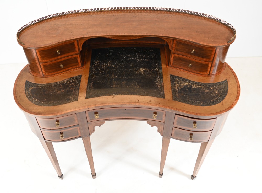 An Edwardian mahogany kidney-shaped writing desk featuring a brass gallery top, inlaid drawers, black leather writing inserts, and tapered legs. View VII