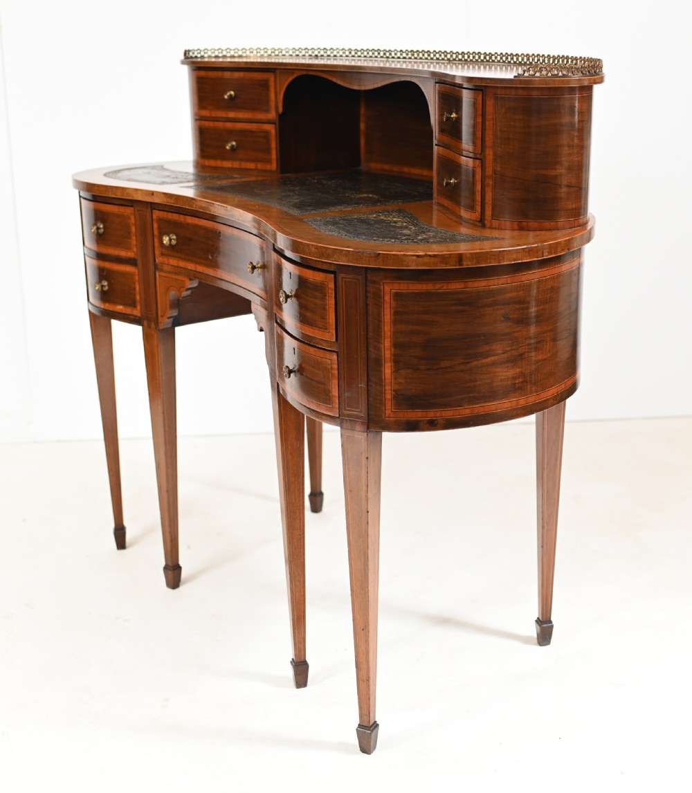 An Edwardian mahogany kidney-shaped writing desk featuring a brass gallery top, inlaid drawers, black leather writing inserts, and tapered legs. View IX