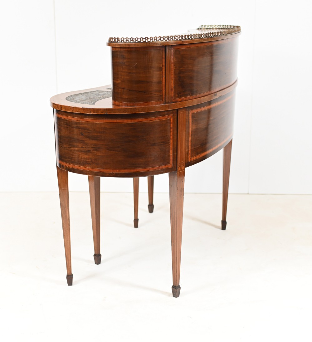 An Edwardian mahogany kidney-shaped writing desk featuring a brass gallery top, inlaid drawers, black leather writing inserts, and tapered legs. View XII